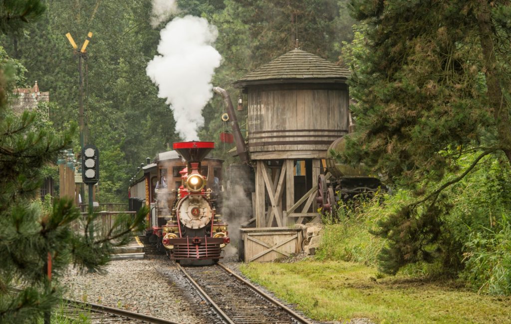 A locomotive is stopped near a water tank. Smoke is coming out of the locomotive