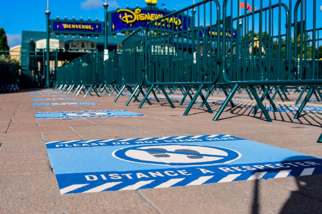 Des barrières vertes canalisent les visiteurs devant l'entrée de Disneyland Paris. Des marquages ont été posés au sol pour respecter les distances de sécurités